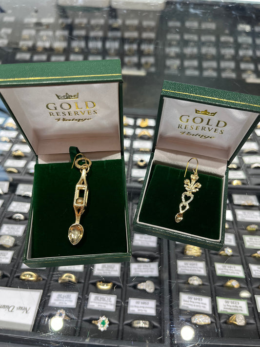 9ct Gold Lovespoon Pendants in green jewellery boxes on a counter with gold vintage rings