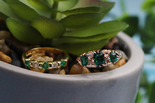 Two gold diamond & emerald rings in a faux plant