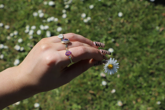 a hand holding a daisy flower with three 9ct gold vintage rings which are amethyst and diamond, a purple stone and a heart signet ring