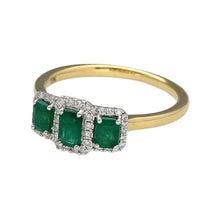 Load image into Gallery viewer, New 18ct Yellow and White Gold Diamond &amp; Emerald Halo Trilogy Ring in size M with the weight 3 grams. The center stone is 5mm by 3mm and the side stones are each 4mm by 3mm. There is approximately 14pt of diamond content set in the ring
