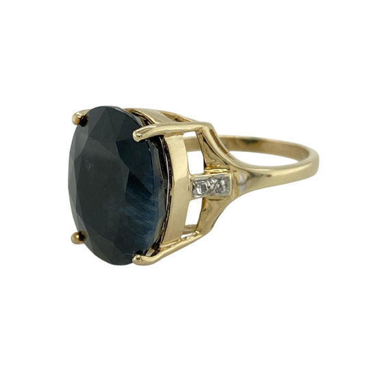 Bring dramatic colour and refined sparkle to your jewellery collection with this pre-owned 9ct yellow gold midnight blue sapphire and white topaz set ring.
Design: The ring features a striking oval midnight blue sapphire at the centre, measuring approximately 16mm by 12mm, creating a bold and luxurious focal point, with white topaz stones set along the shoulders for added brilliance.