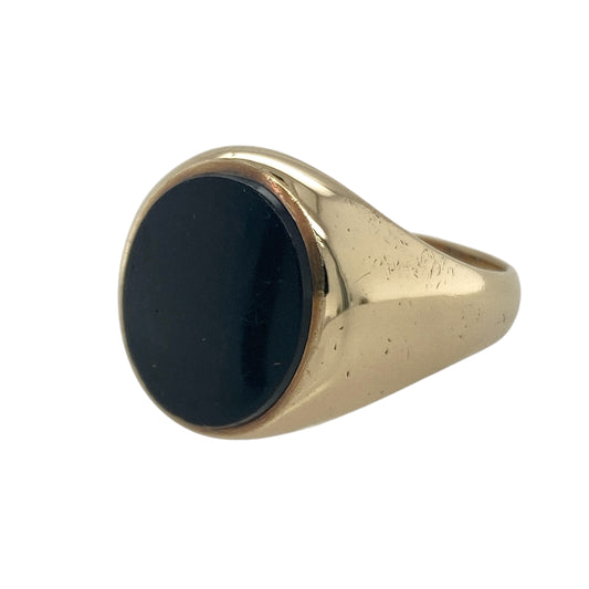 Bring bold sophistication and timeless style to your collection with this pre-owned 9ct yellow gold onyx signet ring—a classic piece that combines strong contrast with refined design.
Design: The ring features an oval-shaped onyx gemstone measuring 13mm by 11mm, showcasing a deep black hue that symbolises strength and elegance. Its smooth, polished surface creates a striking centrepiece against the rich gold setting.