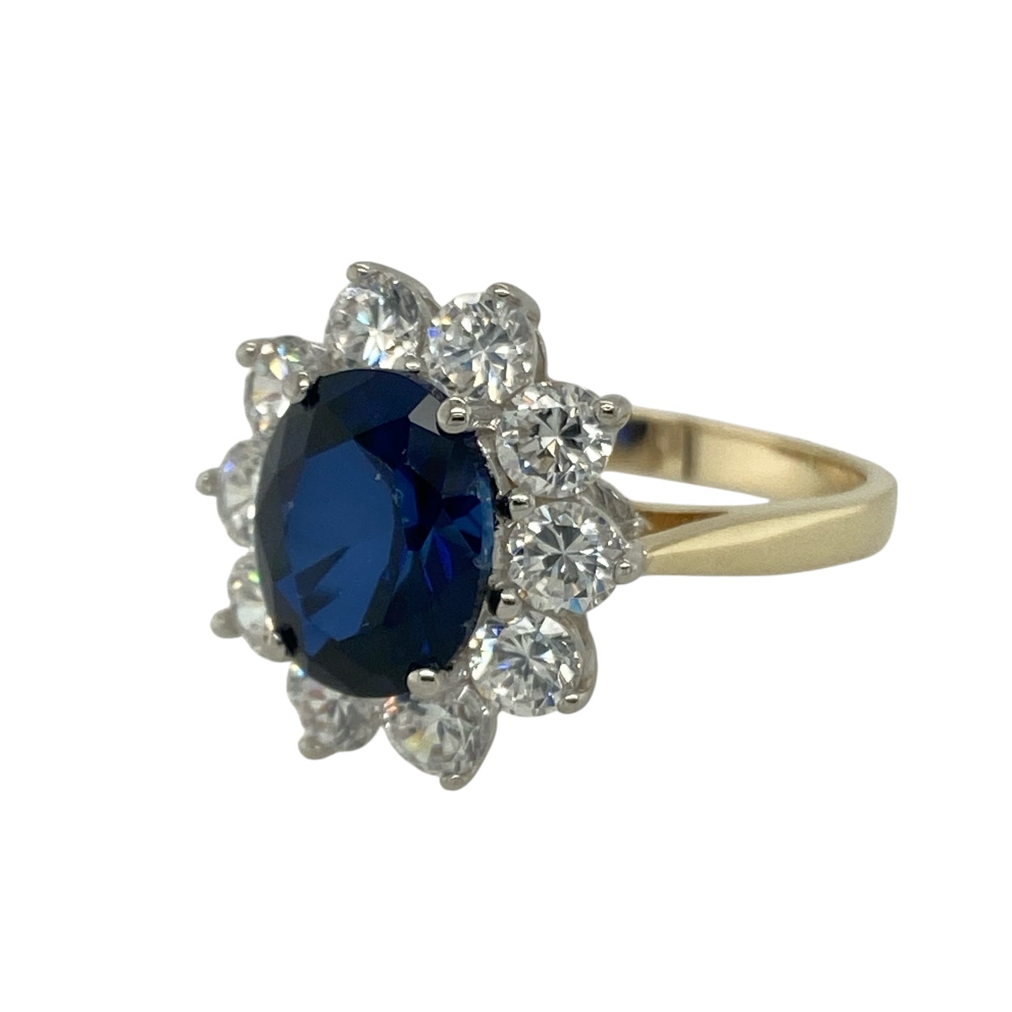 Bring vibrant colour and sparkling elegance to your collection with this pre-owned 9ct yellow gold blue stone and cubic zirconia cluster ring—a classic design that radiates timeless beauty.
Design: The ring features a striking sapphire-coloured oval centre stone measuring 10mm by 8mm, surrounded by a halo of glittering cubic zirconia that enhance its rich blue tone and create a brilliant, eye-catching effect.