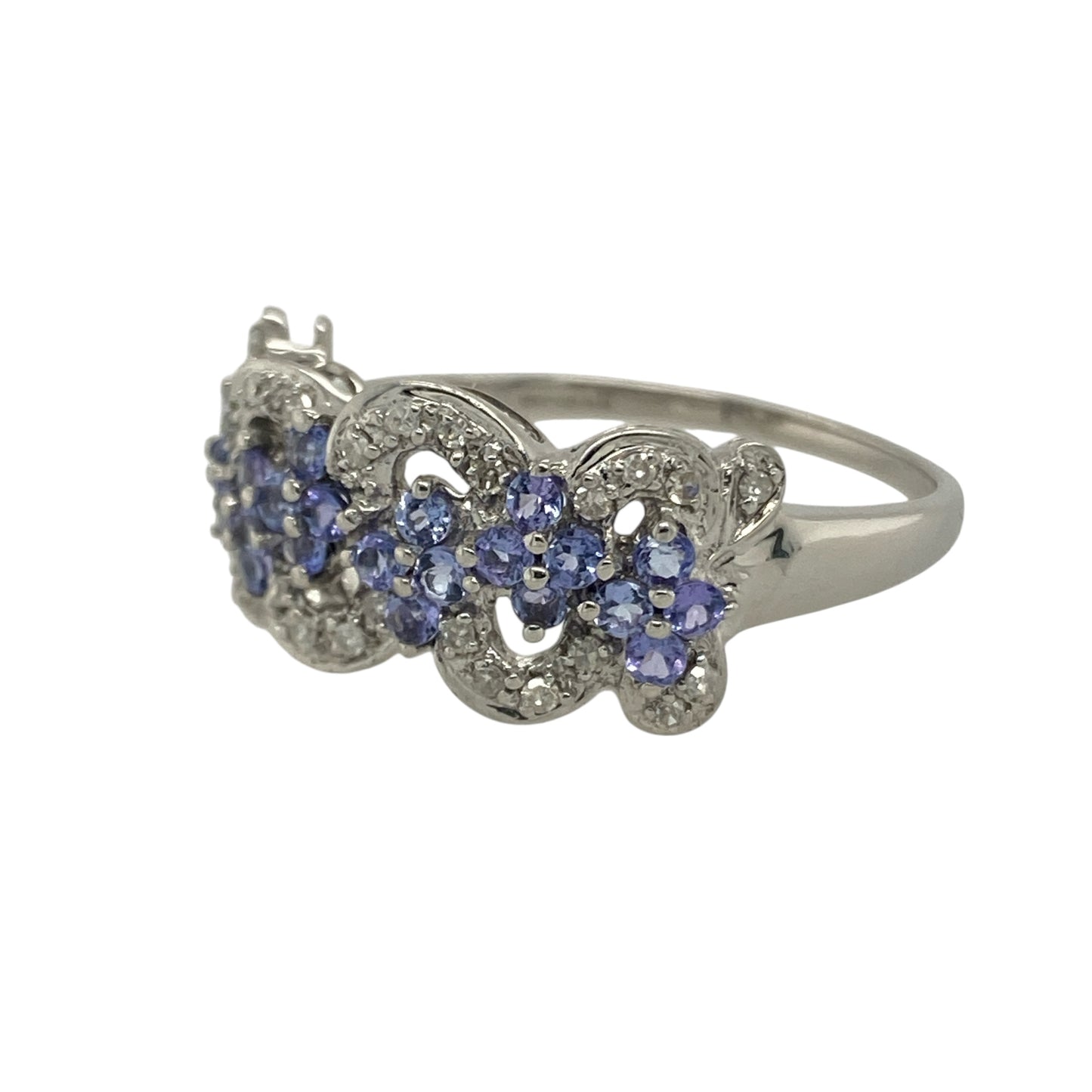 Bring colour, sparkle, and graceful design to your collection with this pre-owned 9ct white gold diamond and tanzanite flower cluster swirl ring—a striking piece that captures elegance with a modern twist.
Design: The ring features a flower-shaped cluster of violet-blue tanzanite stones surrounded by sparkling diamonds, all arranged in a flowing swirl pattern that enhances the ring’s movement and brilliance. The combination of soft colour and sparkle creates a refined, feminine look.