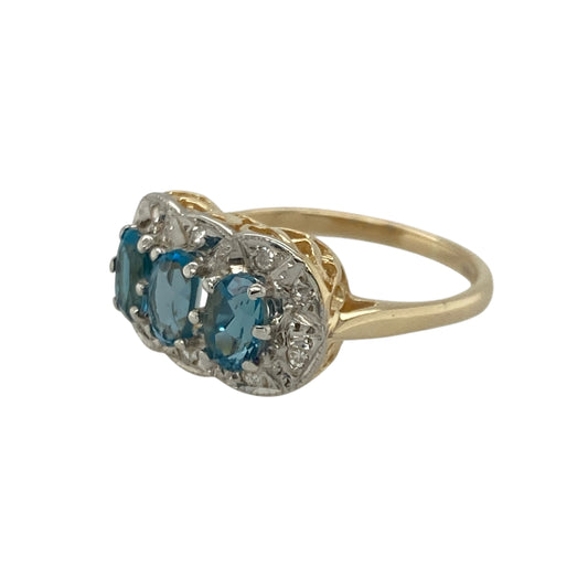 Bring radiant colour and elegant sparkle to your collection with this pre-owned 9ct yellow gold diamond and blue topaz set trilogy cluster ring — a graceful design that captures timeless sophistication.
Design: The ring showcases three oval-cut blue topaz stones, each measuring 5mm by 3mm, surrounded by a halo of shimmering diamonds that enhance their cool, sky-blue brilliance. The trilogy arrangement symbolises past, present, and future, adding a touch of meaning to its refined beauty.