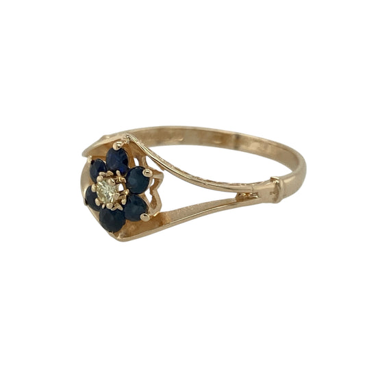 Add a touch of classic sparkle and delicate charm to your collection with this pre-owned 9ct yellow gold diamond and sapphire set flower split band ring — a graceful design that blends timeless beauty with a feminine touch.
Design: The ring features a floral cluster at the centre, formed by rich blue sapphires surrounding a sparkling diamond, with a split band that enhances its elegant and airy appearance. The front of the ring measures 10mm high, giving it a refined yet eye-catching presence.