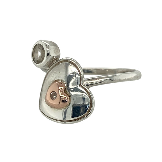 Express love and sparkle with this pre-owned 925 silver and 9ct rose gold Clogau wrap-around heart ring, blending elegant design with sentimental charm—perfect for everyday wear or as a meaningful gift.
Design: The ring features an open wrap-around heart motif measuring 16mm high from top to bottom, adorned with a 4mm round white topaz stone that adds a touch of radiant brilliance.
