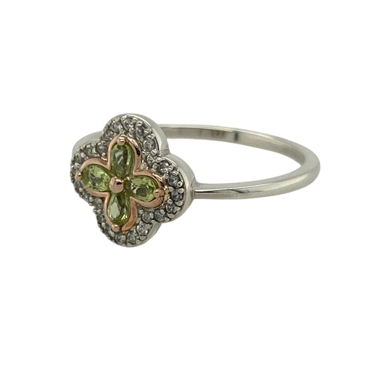 Bring vintage charm and delicate colour to your collection with this pre-owned 925 silver with 9ct rose gold white topaz and peridot set Tudor-style flower cluster Clogau ring—a graceful piece inspired by classic design and natural beauty.
Design: The ring features a central peridot gemstone surrounded by sparkling white topaz stones arranged in a Tudor-style flower cluster, accented with subtle rose gold detailing for added warmth and elegance.
