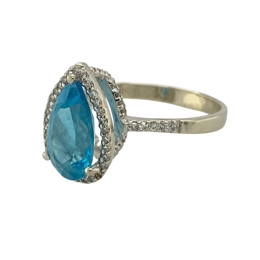 Bring graceful sparkle and a soft wash of colour to your jewellery collection with this pre-owned 9ct white gold diamond & blue topaz halo ring, a refined design that balances elegance with everyday wearability—perfect for special moments or timeless daily luxury.
Design: The ring features a pear-shaped (teardrop) blue topaz measuring 12mm by 7mm, surrounded by a shimmering halo of diamonds, with additional diamonds continuing along the shoulders for added brilliance.