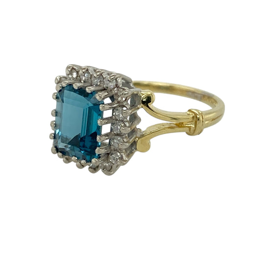 Bring elegant colour and refined sparkle to your jewellery collection with this pre-owned 18ct yellow gold diamond & blue topaz set cluster ring, a timeless design with classic appeal.
Design: The ring features a rectangular blue topaz stone measuring 8mm by 6mm, forming a striking focal point, surrounded by a cluster of diamonds that enhance the colour and add radiant sparkle.