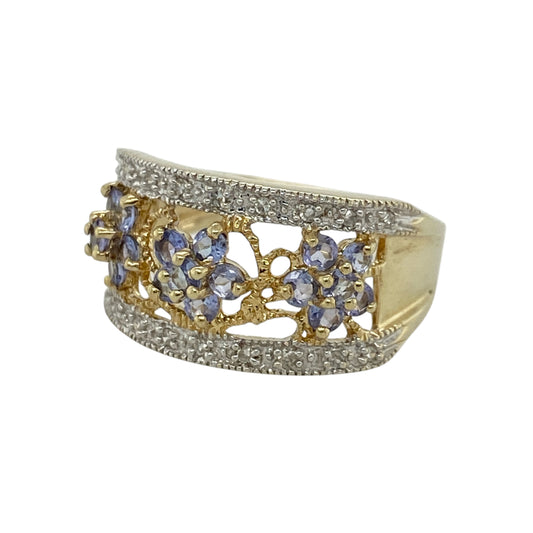 Add bold colour and elegant sparkle to your jewellery collection with this pre-owned 9ct yellow and white gold diamond and tanzanite set wide band ring—an eye-catching statement piece perfect for special occasions or standout everyday wear.
Design: This ring features an impressive 11mm wide front, showcasing three tanzanite flower clusters that create vibrant focal points, with white gold set diamonds positioned either side for added brilliance and balance.