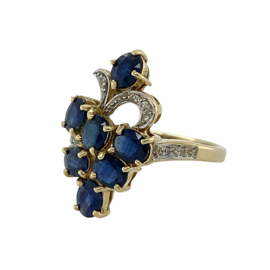 dd bold elegance and rich colour to your jewellery collection with this pre-owned 9ct yellow gold diamond and sapphire set cluster ring—an eye-catching statement piece perfect for special occasions.
Design: This ring features an impressive 22mm high cluster front, set with oval sapphire stones measuring approximately 5mm by 4mm, creating a striking and vibrant focal point. Sparkling diamonds are set both within the cluster and along the shoulders for added brilliance.