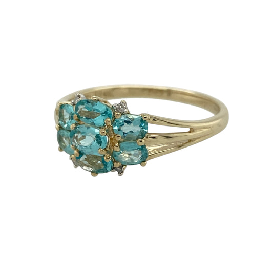 Add vibrant colour and elegant sparkle to your jewellery collection with this pre-owned 9ct yellow gold diamond and blue stone cluster ring, featuring a bold and eye-catching design—perfect for special occasions or standout everyday wear.
Design: The ring features a cluster of seven oval blue stones, each measuring approximately 5mm by 3mm, arranged to create a striking floral-style formation, with small diamonds set around the edges adding extra brilliance.