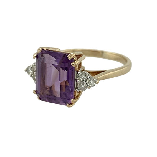Add bold colour and elegant sparkle to your jewellery collection with this pre-owned 9ct yellow gold diamond and amethyst ring, featuring a striking centre stone and refined detailing—perfect for special occasions or statement wear.
Design: The ring showcases a rectangular amethyst measuring approximately 11mm by 9mm at its centre, complemented by small diamond clusters on either side that add brilliance and balance.