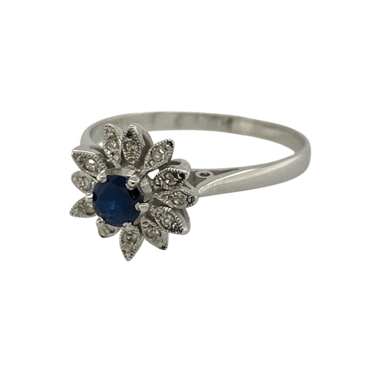 Add timeless elegance and rich colour to your jewellery collection with this pre-owned 18ct white gold diamond and sapphire flower cluster ring, featuring a beautiful floral-inspired design with luxurious sparkle—perfect for special occasions, gifting, or sophisticated everyday wear.
Design: The ring showcases a vibrant round sapphire centre stone measuring approximately 4mm in diameter, surrounded by sparkling diamonds in an elegant flower cluster arrangement