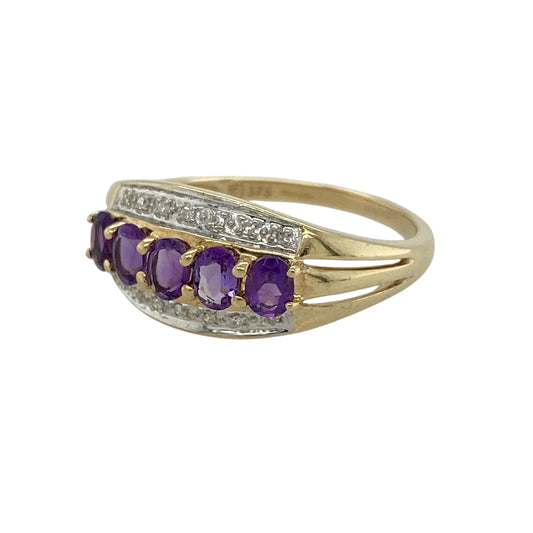 Add vibrant colour and timeless elegance to your jewellery collection with this pre-owned 9ct yellow gold diamond and amethyst band ring, featuring five beautiful oval amethysts framed by sparkling diamond accents.
Design: The ring showcases a striking 10mm wide band across the front, set with five oval-cut amethyst gemstones, each measuring approximately 5mm by 3mm.