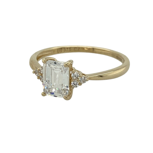 Bring classic elegance and eye-catching sparkle to your jewellery collection with this pre-owned 9ct yellow gold cubic zirconia solitaire ring, featuring a rectangular centre stone with smaller cubic zirconia clusters on each shoulder—perfect as a dress ring, engagement-style ring, or thoughtful gift.
Design: The ring features a rectangular solitaire-style centre stone, complemented by a small cluster of cubic zirconia stones on either side for added sparkle and a beautifully balanced finish.