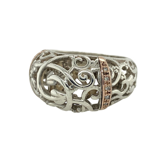 This pre-owned Clogau Tree of Life rounded band ring is a striking sterling silver and 9ct rose gold design, finished with sparkling diamond detail.
Design: Featuring Clogau’s iconic Tree of Life motif across a bold rounded band, this ring combines polished sterling silver with signature 9ct rose gold detailing and a sparkling diamond accent. Measuring approximately 13mm wide across the front, the substantial design beautifully showcases the flowing Tree of Life pattern inspired by Welsh heritage.