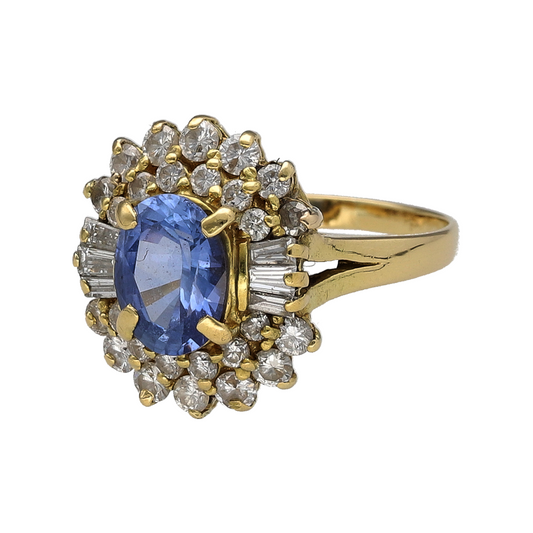 Make a sophisticated statement with this pre-owned 18ct yellow gold diamond and sapphire cluster ring, featuring a beautiful light sapphire-coloured centre stone surrounded by a stunning combination of brilliant and baguette-cut diamonds.
Design: The ring showcases an elegant oval light sapphire-coloured stone measuring approximately 8mm by 6mm, creating a graceful focal point.