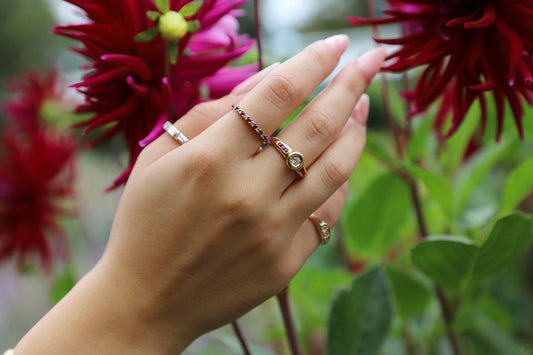 Hand wearing gold rings against a floral background.