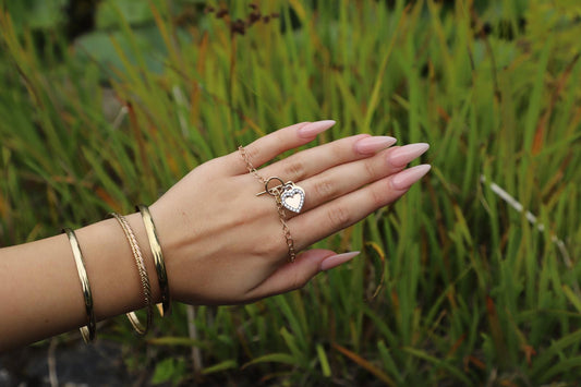 Hand wearing a gold heart bracelet with matching gold bangles.
