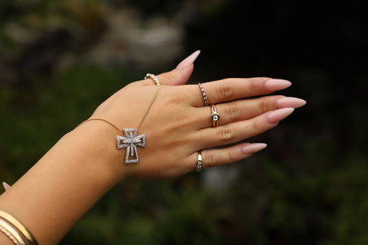 Model wearing a diamond cross pendant necklace with gold rings