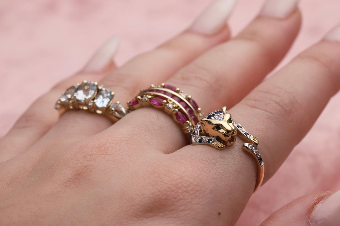 Three 9ct Gold rings on a hand which are a 9ct Gold Diamond & Aquamarine three stone ring, a ruby and diamond 9ct Gold band ring and a 9ct Gold Diamond & Sapphire leopard wrap around ring