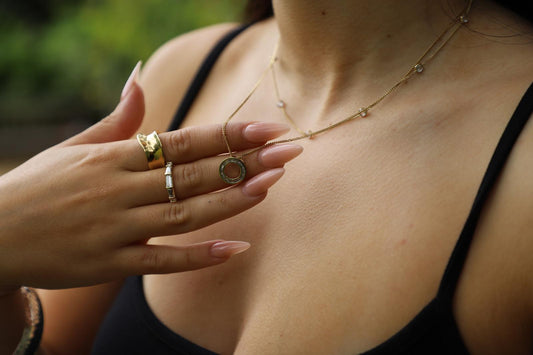 Model wearing a gold pendant necklace with gold rings