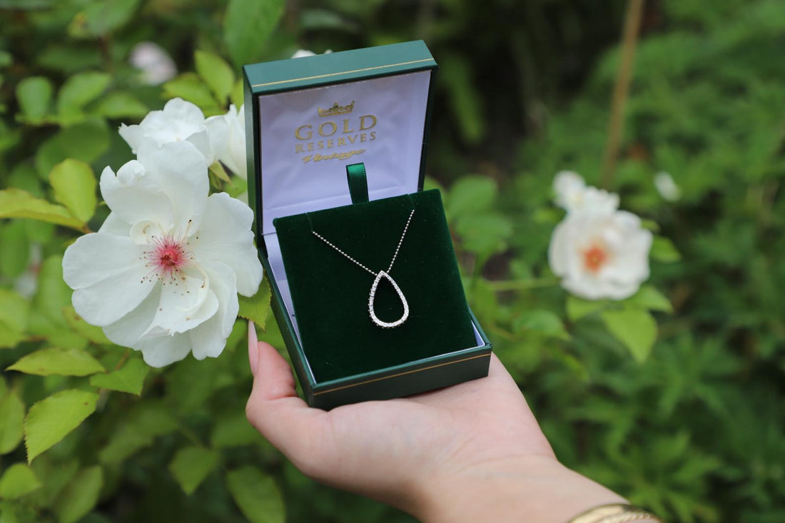 Hand holding white gold diamond set necklace on floral background