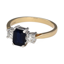 Load image into Gallery viewer, Bring classic elegance and rich colour to your jewellery collection with this new 9ct yellow gold diamond and sapphire trilogy ring—a timeless piece with striking gemstones and refined sparkle.

Design: Featuring a 7mm by 5mm emerald-cut sapphire at the centre, flanked by two brilliant-cut diamonds totalling approximately 0.40ct, the trilogy layout offers a balanced and sophisticated look.

