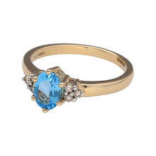 Load image into Gallery viewer, Bring vibrant colour and refined sparkle to your collection with this new 9ct yellow gold diamond and blue topaz set ring, offering a stunning blend of classic elegance and luxurious detail—perfect for adding a statement touch to any look.

Design: The ring features a striking oval blue topaz stone measuring 7mm by 5mm at the centre, accented by three small diamonds on each side, with approximately 0.11ct of total diamond content, creating a bright and captivating focal point.

