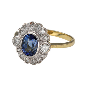 Preowned 18ct Yellow and White Gold Diamond & Sapphire Set Cluster Ring in size L with the weight 3.80 grams. The cornflower blue sapphire is 7mm by 5mm. There is approximately 18pt - 20pt of diamond content set in the ring 