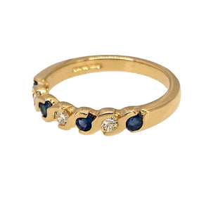 Preowned 18ct Yellow Gold Diamond & Sapphire Set Band Ring in size L with the weight 3 grams. The ring is made up of three brilliant cut diamonds and four round cut sapphires set in a wave style band. There is approximately 12pt - 15pt of diamond content and the sapphire stones are each 2mm diameter 