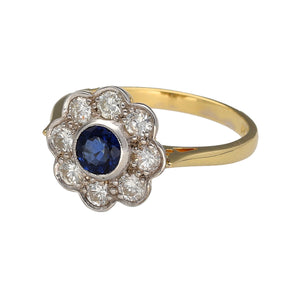 Preowned 18ct Yellow and White Gold Diamond & Sapphire Set Daisy Flower Cluster Ring in size P with the weight 4.30 grams. There is approximately 25pt - 32pt of diamond content set in the ring. The sapphire stone is round cut and is 5mm diameter