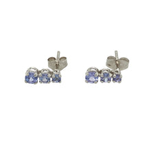 Load image into Gallery viewer, Bring delicate colour and elegant sparkle to your collection with these pre-owned 9ct white gold and tanzanite set three stone stud earrings, offering graceful design and soft violet hues—perfect for refined everyday wear or thoughtful gifting.

Design: Each earring features a vertical trio of round tanzanite stones, graduating in size from top to bottom, with the largest stone measuring 3mm in diameter, creating a subtle cascading effect.

