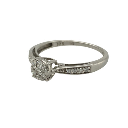 Bring timeless sparkle and elegant style to your collection with this pre-owned 9ct white gold diamond cluster illusion-set solitaire ring—a refined design that captures brilliance and sophistication.

Design: The ring features an illusion-set cluster of brilliant-cut diamonds at the centre, creating the appearance of a larger single stone with enhanced sparkle. Additional diamonds are set along the shoulders, adding extra radiance and a touch of luxury.