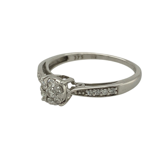 Bring timeless sparkle and elegant style to your collection with this pre-owned 9ct white gold diamond cluster illusion-set solitaire ring—a refined design that captures brilliance and sophistication.

Design: The ring features an illusion-set cluster of brilliant-cut diamonds at the centre, creating the appearance of a larger single stone with enhanced sparkle. Additional diamonds are set along the shoulders, adding extra radiance and a touch of luxury.