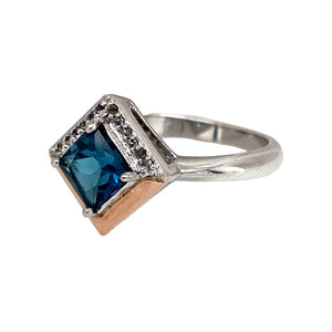 Bring romantic sparkle and elegant colour to your collection with this pre-owned 925 silver and 9ct rose gold Clogau blue topaz and cubic zirconia Kensington Love ring, offering a refined blend of delicate design and modern charm—perfect for adding a touch of romance to any look.

Design: The ring features a striking 6mm by 6mm blue topaz at its centre, accented by shimmering cubic zirconia stones that enhance its brilliance and create a graceful, feminine silhouette.
