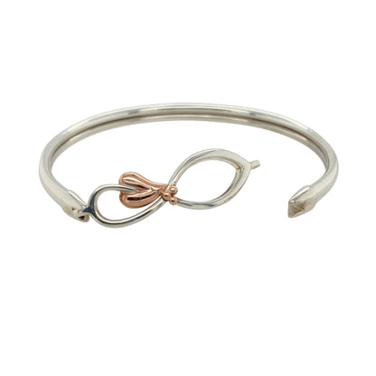 Add a symbol of eternity and elegance to your jewellery collection with this pre-owned 925 silver with 9ct rose gold Clogau Tree of Life infinity bangle.

Design: Featuring the iconic Tree of Life infinity symbol, this bangle represents eternal love and interconnectedness, beautifully enhanced by 9ct rose gold accents.
Material: Crafted from 925 sterling silver with luxurious 9ct rose gold detailing, this bangle exudes both timeless beauty and quality craftsmanship.
Size & Weight: Weighing 12.10 grams