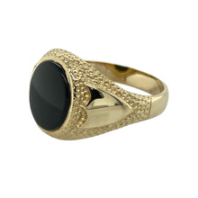 Load image into Gallery viewer, Add bold character to your jewellery collection with this pre-owned 9ct yellow gold and onyx set oval signet ring, featuring:

Design: A classic oval signet style with a deep black onyx centre and detailed shield symbols on the shoulders for a strong, distinguished look.
Material: 9-carat yellow gold, offering a warm, polished finish that enhances the boldness of the design.
Gemstone Detail: Set with a 12mm by 10mm oval onyx stone, creating a striking focal point.
Size &amp; Weight: Designed in size V
