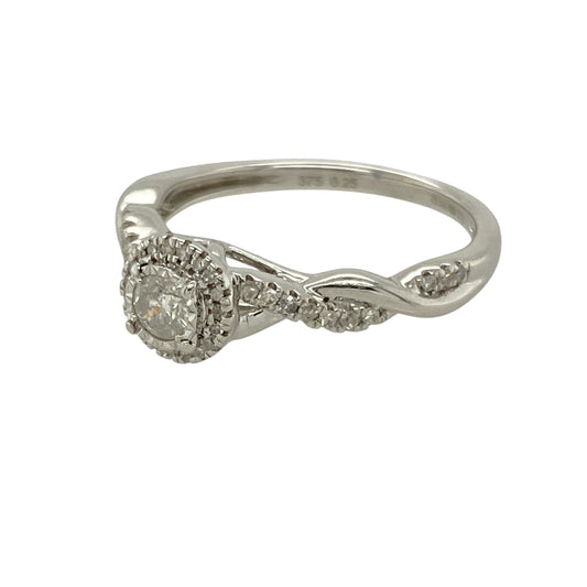 Introduce refined sparkle to your collection with this pre-owned 9ct white gold and diamond set halo ring, designed to dazzle from every angle, featuring:

Design: A graceful halo style, centred around a brilliant diamond and accented by elegantly twisted, diamond-set shoulders for added sophistication.
Material: Crafted in 9-carat white gold, offering a cool-toned, polished finish that beautifully enhances the brilliance of each stone.