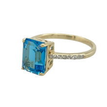 Load image into Gallery viewer, Bring vibrant elegance and refined sparkle to your collection with this pre-owned 9ct yellow gold diamond and blue topaz set ring, featuring a bold centre stone and timeless design—perfect for standout occasions or everyday sophistication.

Design: The ring showcases a striking 9mm by 7mm rectangular blue topaz at the centre, framed by diamond-set shoulders that add brilliance and balance to the vivid blue hue.
Material: Made from 9-carat yellow gold
