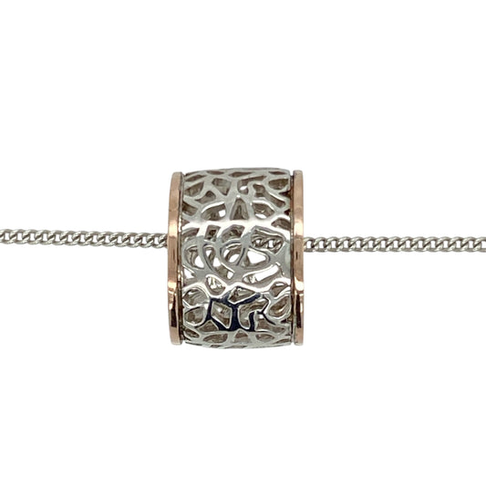 Bring floral elegance and distinctive charm to your collection with this pre-owned 925 silver with 9ct rose gold Clogau rose patterned barrel pendant on an 18" Clogau curb chain, featuring detailed craftsmanship in a bold design—perfect for everyday wear or special gifting.

Design: The pendant features a barrel shape measuring 11mm long and 15mm in diameter, adorned with intricate rose patterns and accented with Clogau’s signature 9ct Welsh rose gold detailing.
