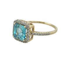 Load image into Gallery viewer, Bring radiant colour and elegant sparkle to your collection with this pre-owned 9ct yellow gold halo ring, featuring a brilliant blue topaz surrounded by diamonds—perfect for refined statement wear or special occasions.

Design: The ring showcases a 7mm by 7mm round blue topaz at the centre, encircled by a halo of diamonds with additional diamonds set along the shoulders for added brilliance and detail.

