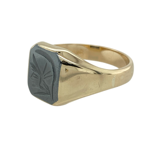 Add bold presence and historical intrigue to your collection with this pre-owned 9ct yellow gold and hematite signet ring, featuring a striking centurion head design—ideal for those who appreciate strong detail and timeless style.

Design: The ring features an 11mm by 9mm rectangular hematite stone engraved with a centurion head, offering a unique focal point with a sense of heritage and strength.

