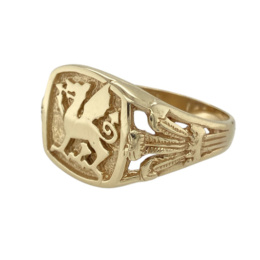 Show your pride and heritage with this pre-owned 9ct yellow gold Welsh dragon signet ring—perfect for those who value bold symbolism and timeless design.

Design: The ring features a 16mm high front with a raised Welsh dragon emblem, flanked by detailed three feather symbols on each shoulder for added meaning and distinction.
Material: Made from 9-carat yellow gold, the polished finish enhances the detailed engraving and adds a rich, traditional glow.
