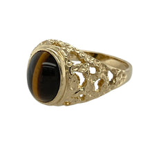 Load image into Gallery viewer, Add natural richness and vintage style to your collection with this pre-owned 9ct yellow gold and tiger’s eye oval signet ring—perfect for bold character with timeless charm.

Design: The ring features a 10mm by 8mm oval tiger’s eye stone, showcasing its golden-brown bands and signature chatoyancy, framed by open patterned shoulders for added visual interest.
Material: Made from 9-carat yellow gold, the polished finish enhances the warm tones of the metal and complements the earthy shimmer of the stone.

