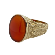 Load image into Gallery viewer, Add bold colour and classic craftsmanship to your collection with this pre-owned 9ct yellow gold and carnelian set patterned oval signet ring—perfect for timeless style with a striking finish.

Design: The ring features a 16mm by 11mm oval carnelian stone with a rich reddish-brown hue, framed by intricately patterned shoulders that enhance its vintage-inspired appeal.
Material: Made from 9-carat yellow gold, the polished finish highlights the warmth of the gold and the depth of the carnelian.


