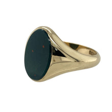 Load image into Gallery viewer, Bring bold character and timeless elegance to your collection with this pre-owned 9ct yellow gold and bloodstone oval signet ring, offering a striking design and refined presence—perfect for making a sophisticated statement.

Design: The ring features a striking oval bloodstone measuring 14mm by 10mm, creating a rich and dramatic focal point. The deep green tones with subtle red flecks give the stone a distinctive and classic appeal, beautifully framed by the warm gold.

