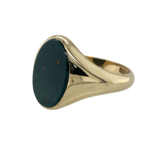 Bring bold character and timeless elegance to your collection with this pre-owned 9ct yellow gold and bloodstone oval signet ring, offering a striking design and refined presence—perfect for making a sophisticated statement.

Design: The ring features a striking oval bloodstone measuring 14mm by 10mm, creating a rich and dramatic focal point. The deep green tones with subtle red flecks give the stone a distinctive and classic appeal, beautifully framed by the warm gold.

